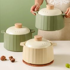 two green pots with wooden lids are sitting on a white table and someone is holding the lid