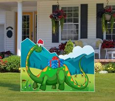 a green dinosaur with a santa hat on standing in front of a house