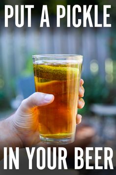 a person holding a glass with liquid in it and the words put a pickle in your beer