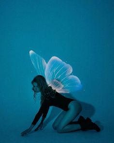 a woman kneeling down in front of a blue background with an angel wings on her back