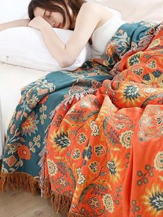 a woman laying in bed with an orange and blue blanket on top of her head