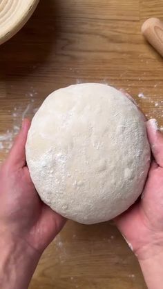 a person holding a ball of dough on top of a wooden table with rolling pins