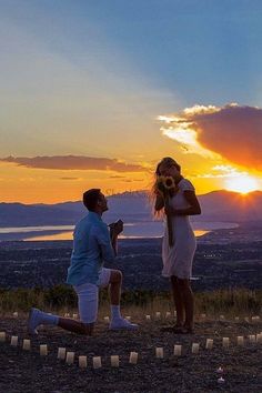 two people standing on top of a hill with candles in front of them and the sun setting behind them