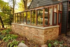 a small brick house in the woods with lots of windows on it's side