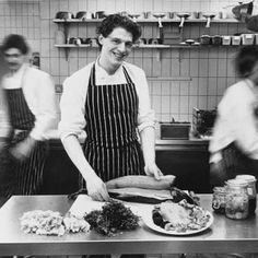 black and white photograph of people in a kitchen preparing food on a table with an apron