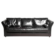 a black leather couch with three pillows on it's back and one arm facing the camera