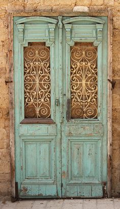 an old blue door with intricate iron work on the doors and side panels, in front of a stone wall