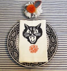 a black and white striped table cloth with an orange flower on top of it next to a cat napkin holder