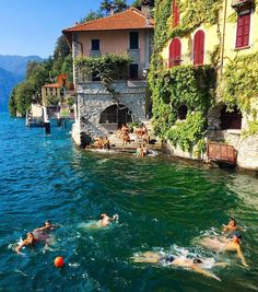 people swimming in the water next to buildings and trees on both sides of the lake