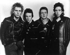 four men standing next to each other in black leather jackets and one man with short hair is looking at the camera