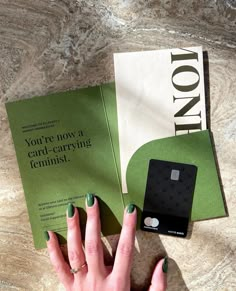 a woman's hand with green nail polish next to a card - carrying item