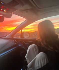 a woman sitting in the driver's seat of a car as the sun sets