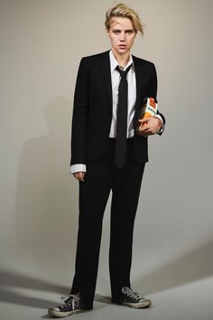 a young man in a suit and tie holding an orange juice box while standing against a white wall