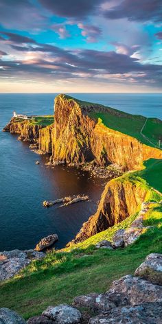 an island in the middle of the ocean with green grass and rocks around it, under a cloudy sky