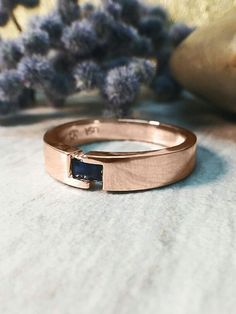 a couple of rings sitting on top of a table next to purple flowers and rocks