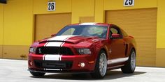 a red and white striped mustang parked in front of a yellow building with two garage doors