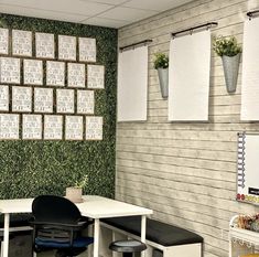 an office cubicle with white tables and black chairs in front of a green wall