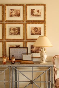 a table topped with pictures and a lamp next to a wall covered in framed pictures