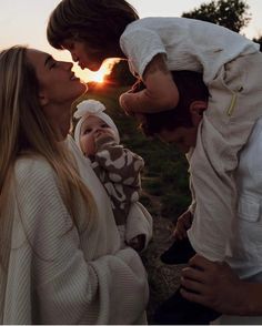 a man and woman holding a baby in their lap as the sun sets behind them