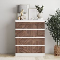 a white and brown chest of drawers next to a potted plant