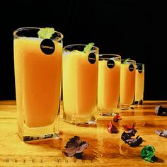 five glasses filled with orange juice on top of a wooden table