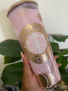 a person holding up a pink starbucks cup with gold trimmings on the side