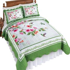 a green and white quilted bed with pink flowers on the comforter, along with two pillows