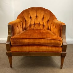 an orange velvet chair sitting on top of a carpeted floor next to a white wall