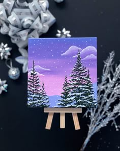 a small easel with a painting on it next to snowflakes and ornaments