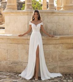 a woman in a white dress leaning against a stone wall