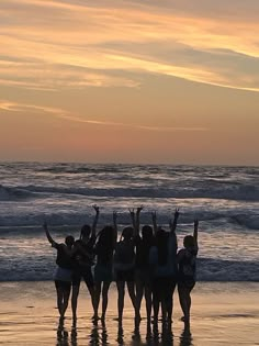 a group of people standing on top of a beach next to the ocean at sunset