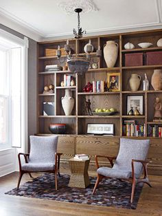 two chairs and a table in front of a bookcase with vases on it