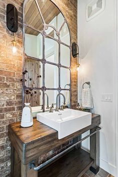 a bathroom sink sitting under a large mirror next to a brick wall in front of a doorway