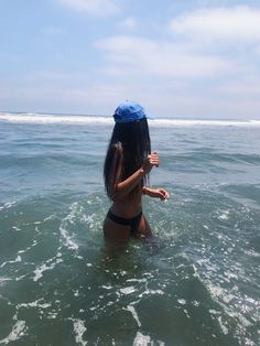 a woman standing in the ocean with an umbrella on her head and holding something up to her face