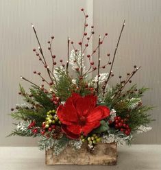 a red flower arrangement in a wooden box with berries and greenery on the side