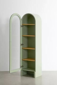 an open green cabinet sitting on top of a cement floor next to a white wall