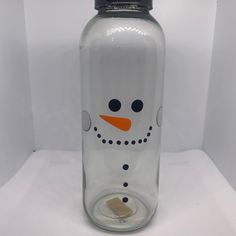 a glass bottle with a snowman face painted on the front and side, sitting on a white surface