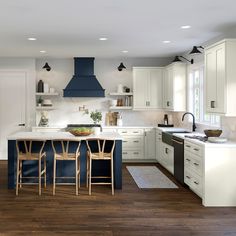 a large kitchen with white cabinets and blue island in the center, along with wooden flooring