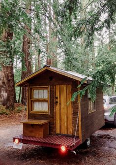 a small wooden cabin sitting in the woods next to a parked car and tree branches