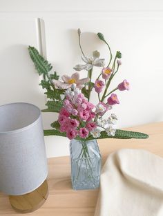 a vase filled with pink and white flowers on top of a wooden table next to a lamp