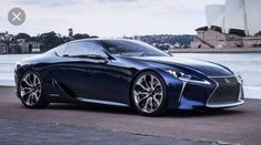 a blue sports car parked in front of the sydney opera house with water behind it