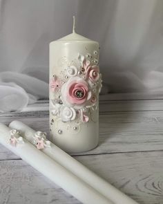 a white candle with pink roses and pearls on it next to a large toothbrush