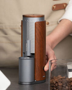 a person is holding a coffee maker over some coffee beans and other things on the table