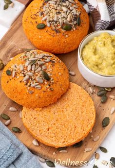 three buns on a wooden board next to a bowl of hummus and pumpkin puree