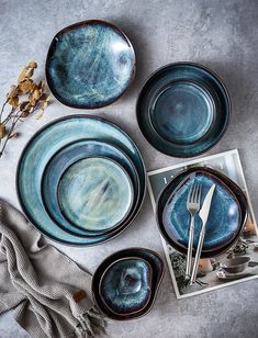 blue plates and silverware are arranged on a gray table cloth, next to a plant