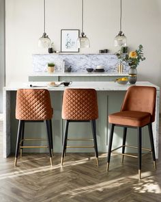 two orange chairs sitting in front of a kitchen island with marble counter tops and bar stools