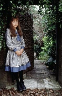 a woman standing in front of an iron gate with leaves on the ground around her