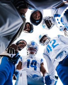 a group of football players standing in a huddle looking up at the camera man