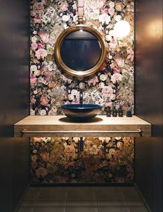 a bathroom with floral wallpaper and a round mirror above the sink in front of it