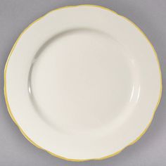 an empty white plate with yellow trim around the edge on a gray surface, ready to be used for serving